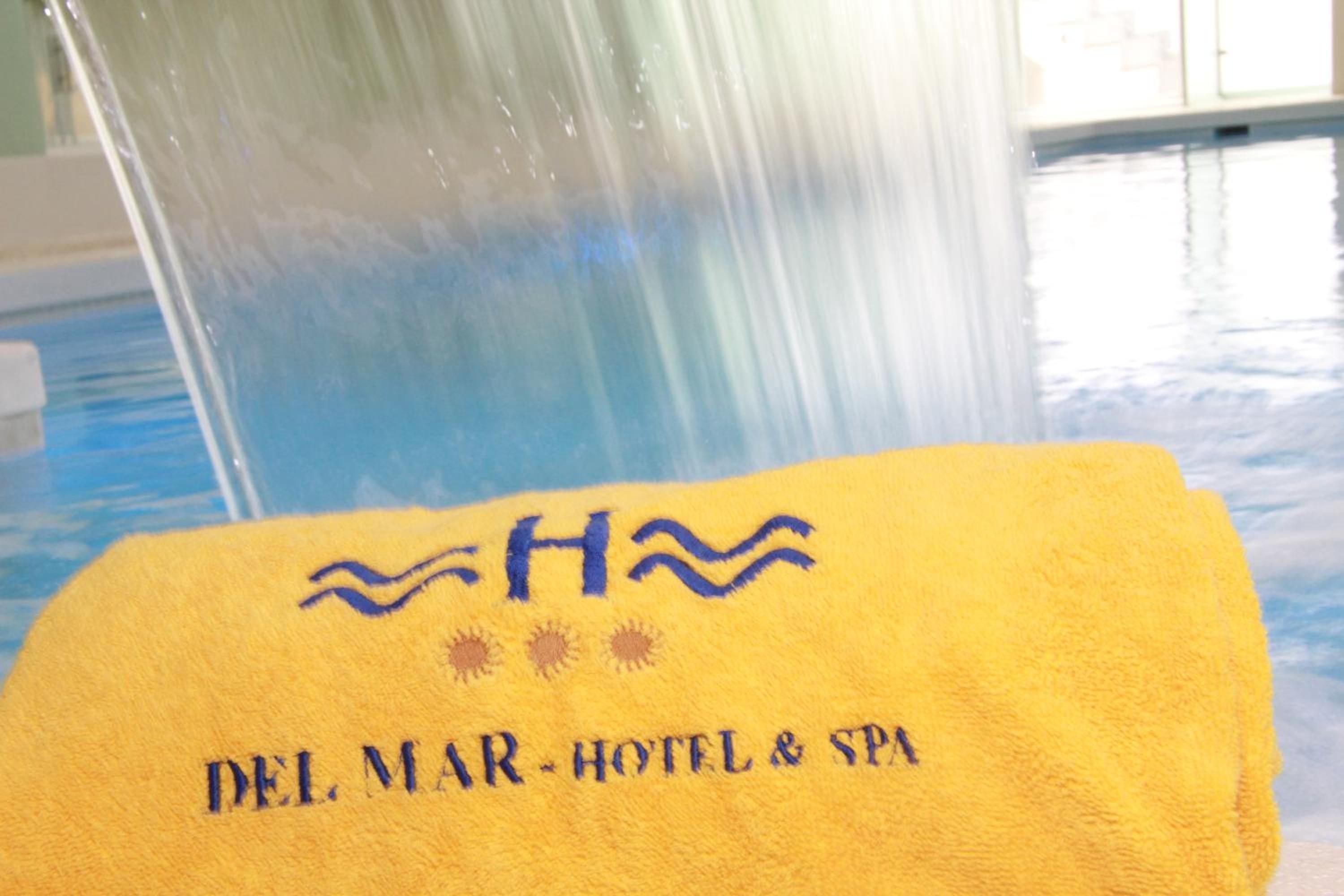 Una toalla amarilla con el texto 'DEL MAR HOTEL & SPA' y un logotipo, ubicada en una zona junto a la piscina.