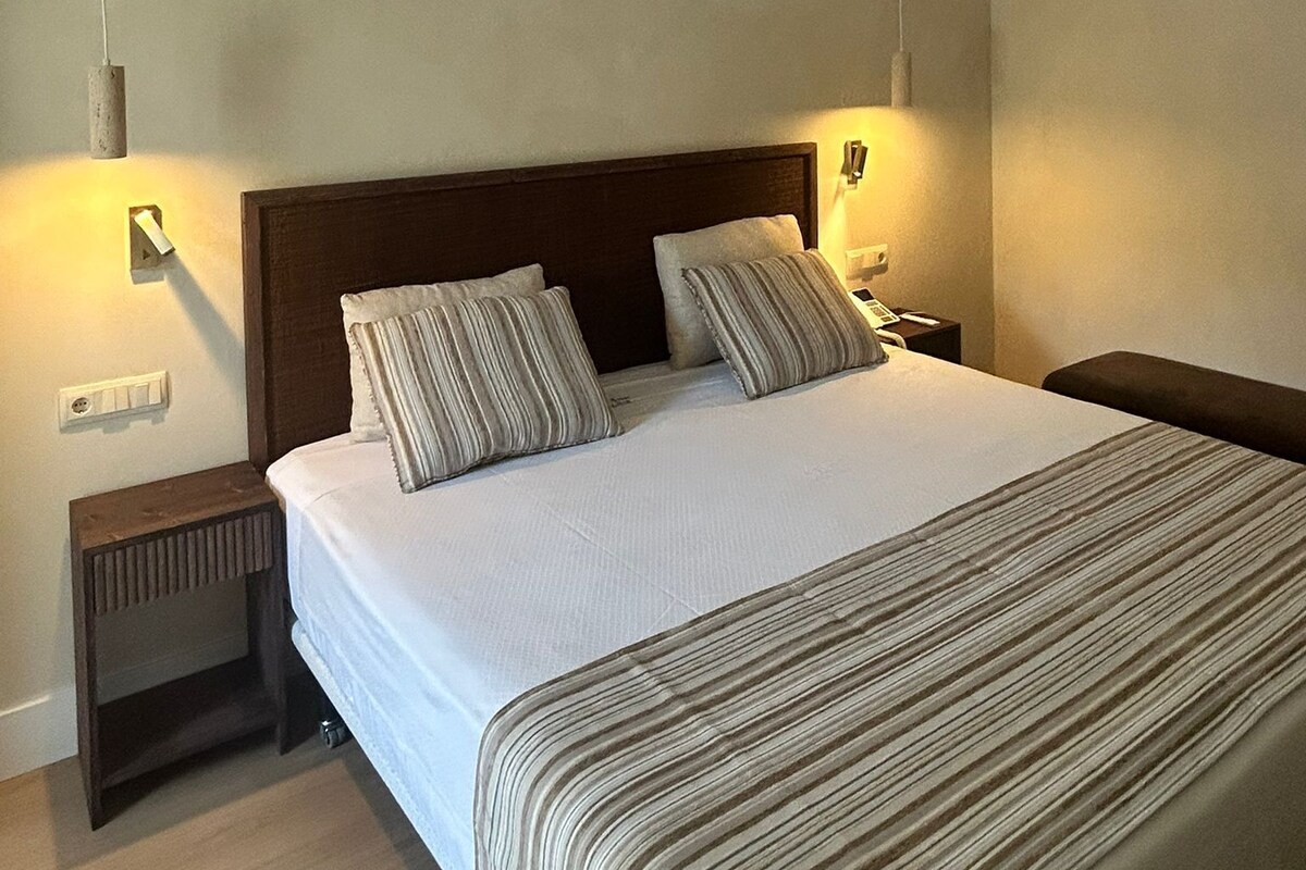 A hotel room with a large bed, two bedside tables, a ceiling fan, and wall-mounted lights.