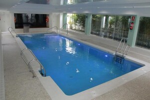 Una piscina interior con agua cristalina, escaleras metálicas y señales de seguridad.