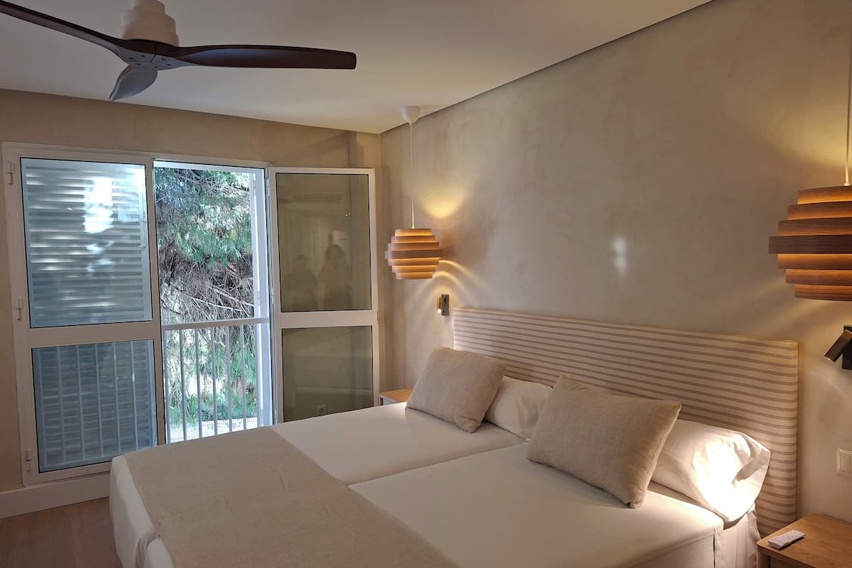 Een slaapkamer met een bed, een plafondventilator, een raam met jaloezieën en een wandlamp.