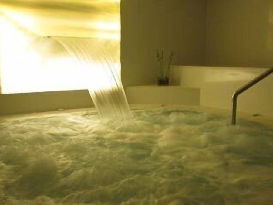 Ein Whirlpool, in den Wasser fließt, eine Badewanne und ein Fenster mit Vorhängen.