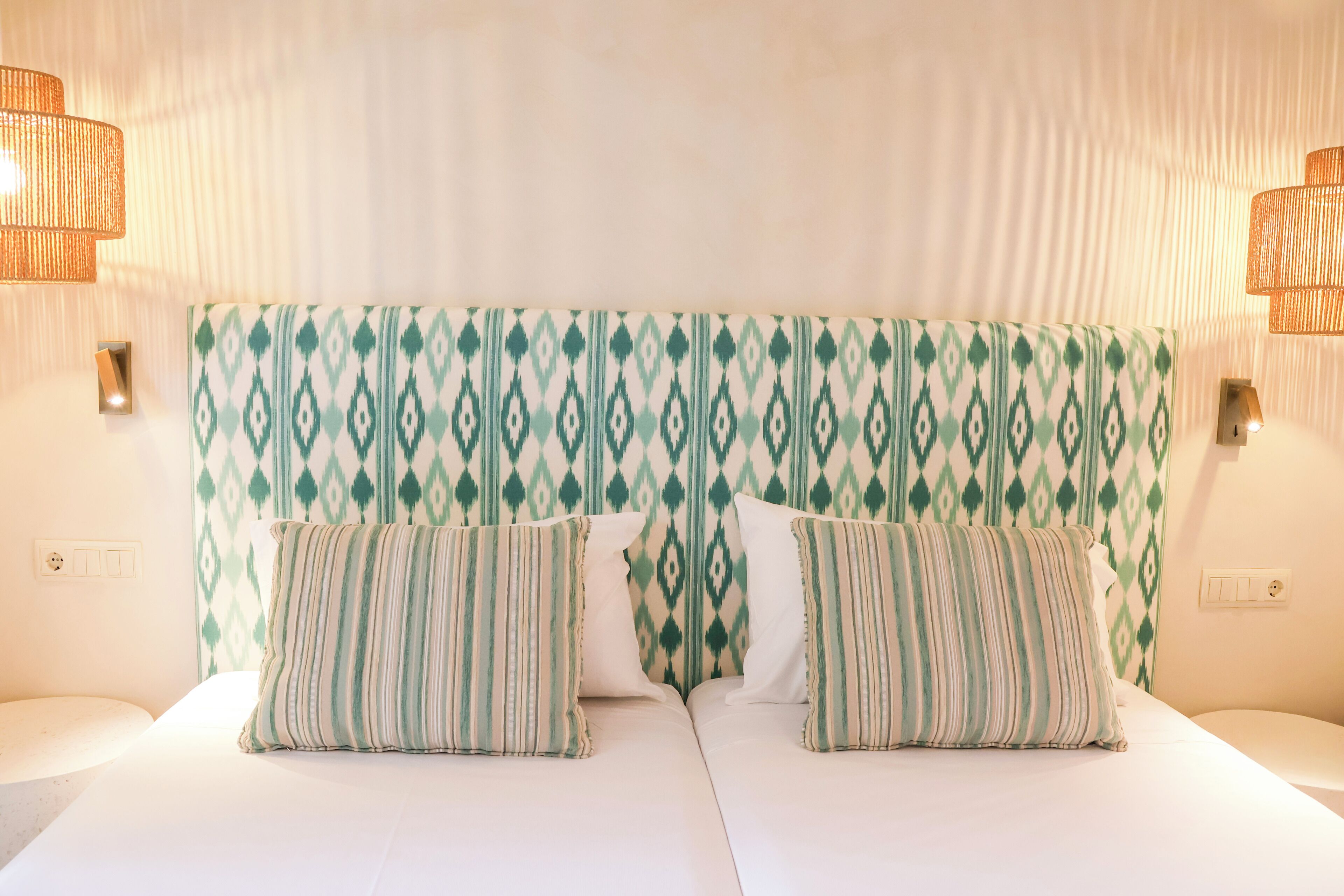 A double bed with a patterned headboard and two pillows, a wall socket, and a light switch.