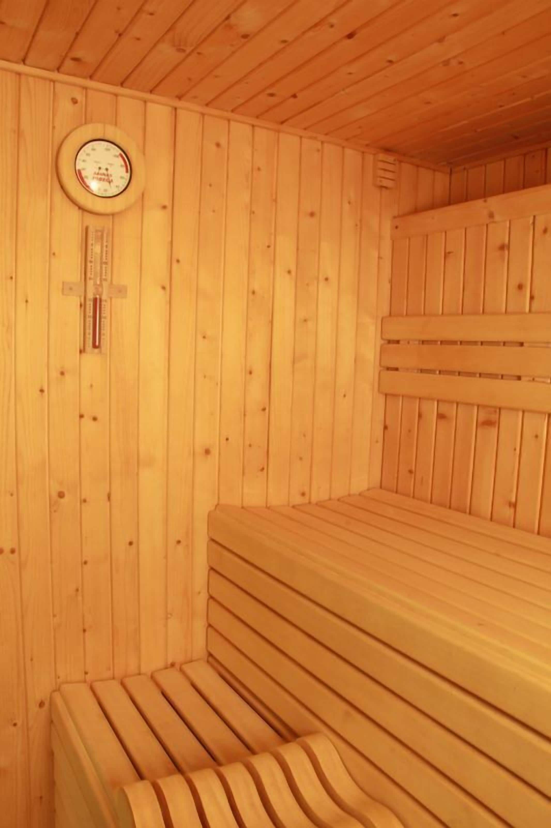 A sauna with wooden benches and a wall-mounted thermometer.