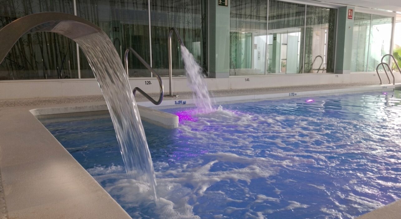 A swimming pool with a water feature, glass walls, and a metal railing.