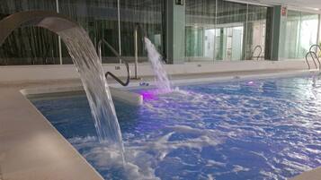 A swimming pool with a water feature, glass walls, and a metal railing.