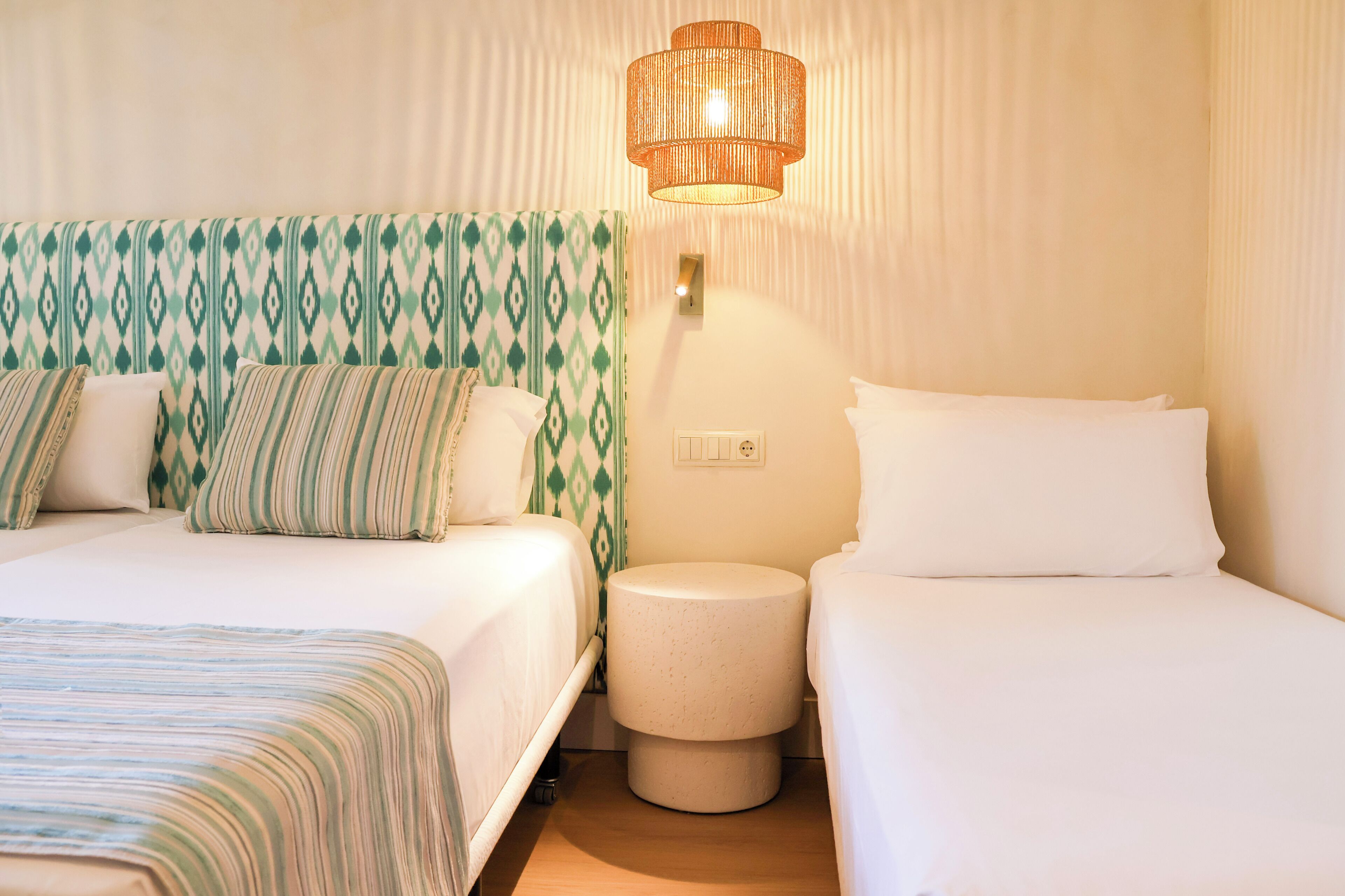A hotel room with two beds, a nightstand, a lamp, and a patterned wall.