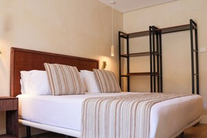 Habitación de hotel con cama, mesita de noche, repisa en la pared y lámpara colgante.