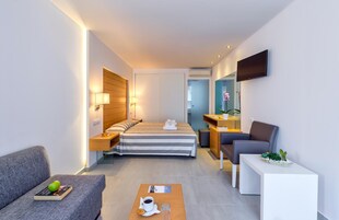 Una habitación de hotel moderna con cama, sofá, escritorio, televisor y mesa de centro.