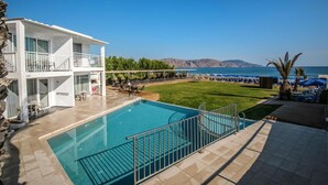 A pool area with a clear view of the sea, a white building with balconies, and a grassy lawn. - Happy Days Hotel (Apokoronas)