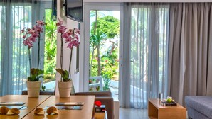 A modern hotel room with a large window, a dining area with a table and chairs, and a sofa. - Happy Days Hotel (Apokoronas)