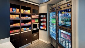 A self-service snack and beverage area with shelves stocked with various snacks and a refrigerated section with bottled drinks. - Courtyard by Marriott Atlanta Downtown (Atlanta)