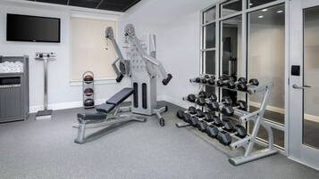A gym with a bench press, dumbbells, and a TV on the wall.