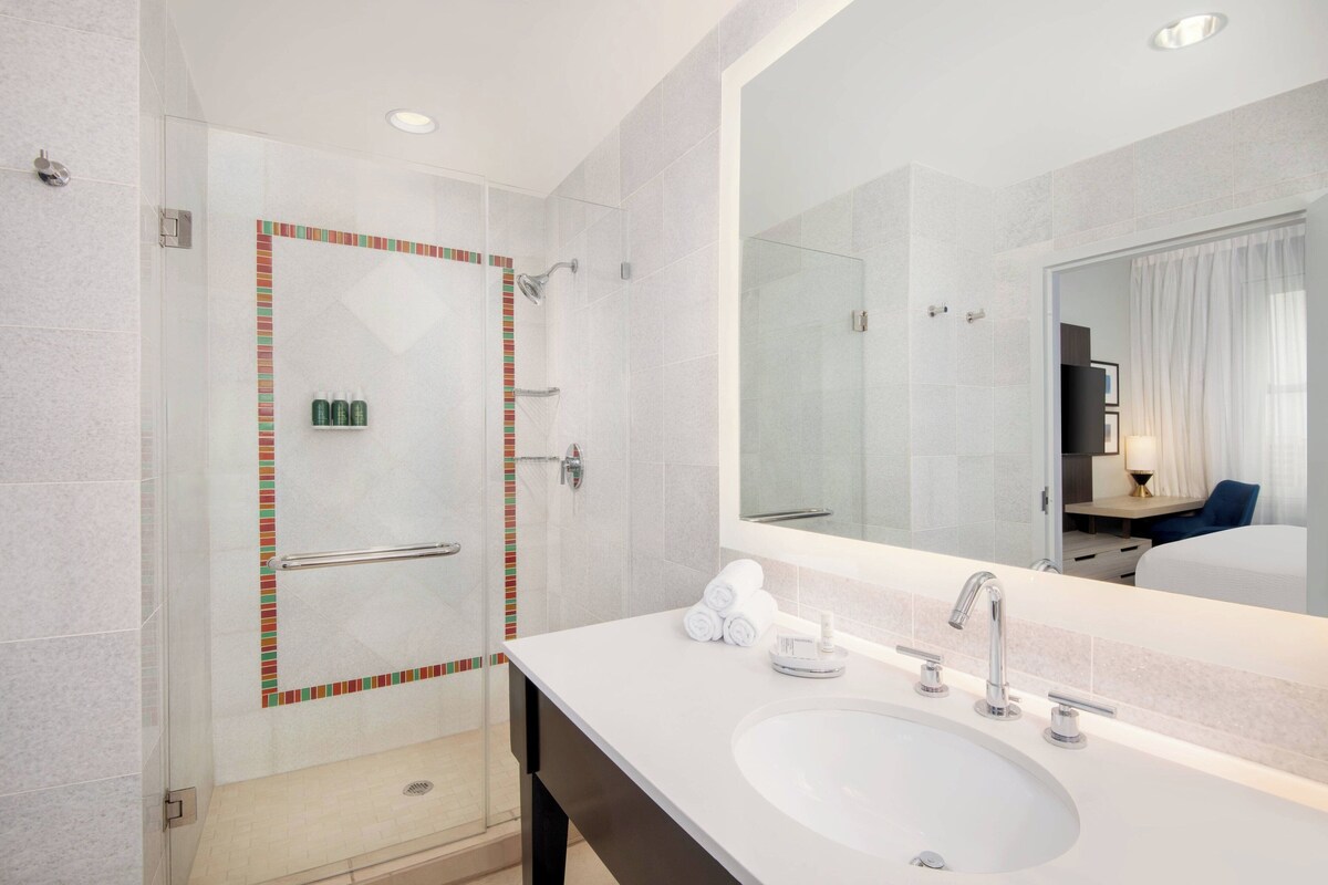 A modern bathroom with a glass-enclosed shower, a white sink, and a large mirror.