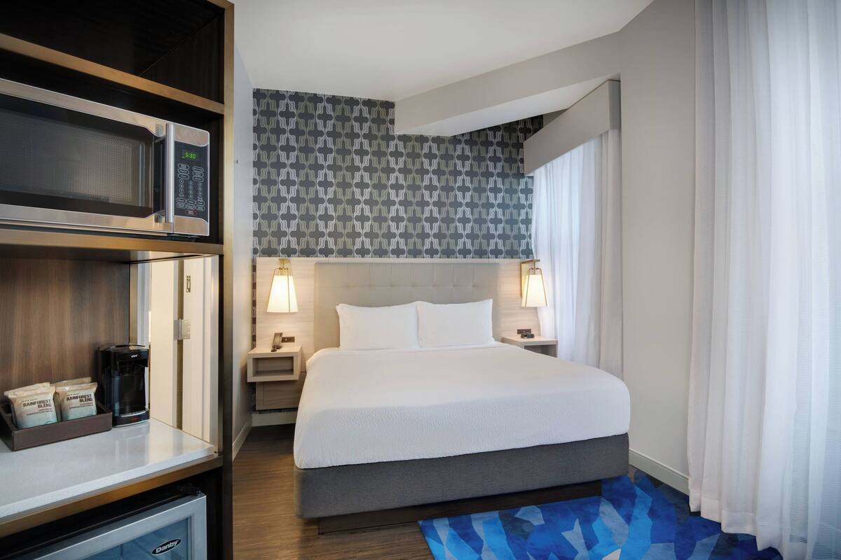 A hotel room with a bed, bedside tables, a microwave, a coffee maker, and a mini-fridge.