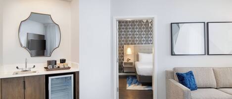 Une chambre d’hôtel moderne équipée d’une kitchenette, d’un lit, d’un canapé et d’une salle de bain avec un miroir et un lavabo.