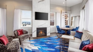 A modern living room with a fireplace, comfortable seating, a dining area, and a large window offering a city view. - Courtyard by Marriott Atlanta Downtown (Atlanta)
