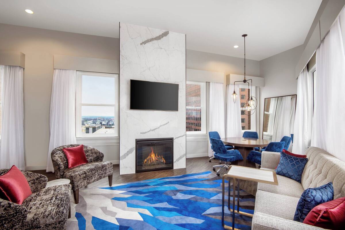 A modern living room with a fireplace, comfortable seating, a dining area, and a large window offering a city view.