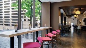 A modern restaurant with a long counter, red cushioned chairs, and large windows offering a view of the cityscape. - Courtyard by Marriott Atlanta Downtown (Atlanta)