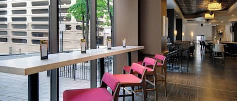 A modern restaurant with a long counter, red cushioned chairs, and large windows offering a view of the cityscape.