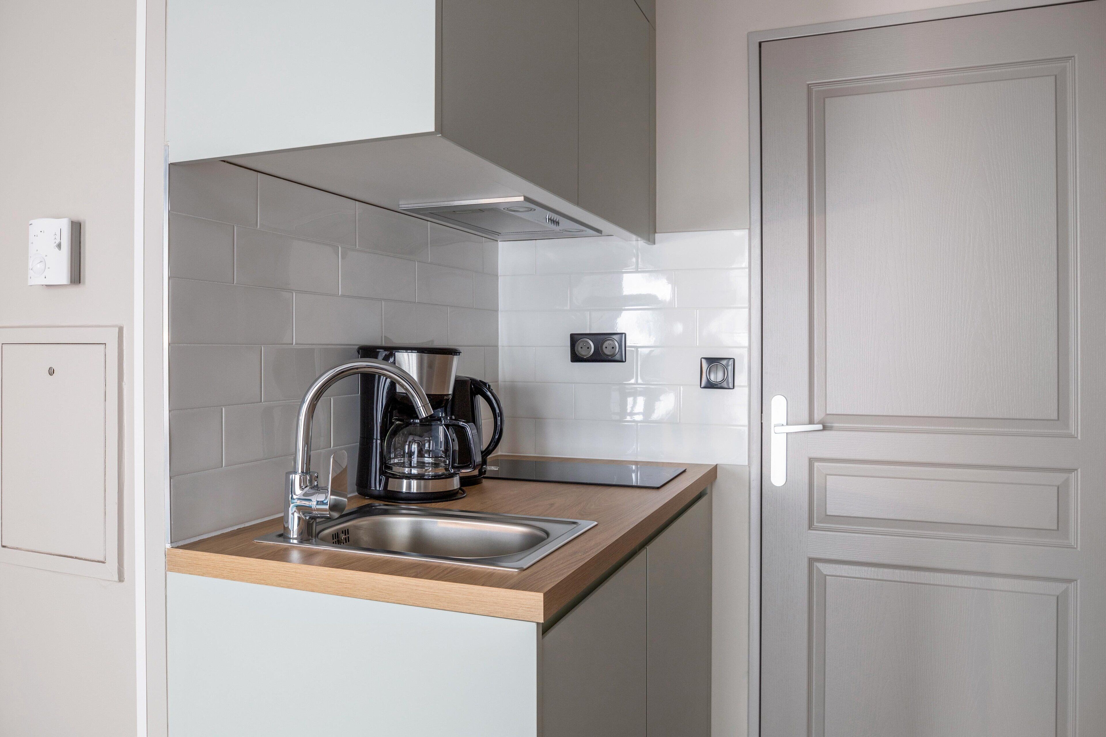 A modern kitchen with a stainless steel sink, a coffee maker, and a range hood.