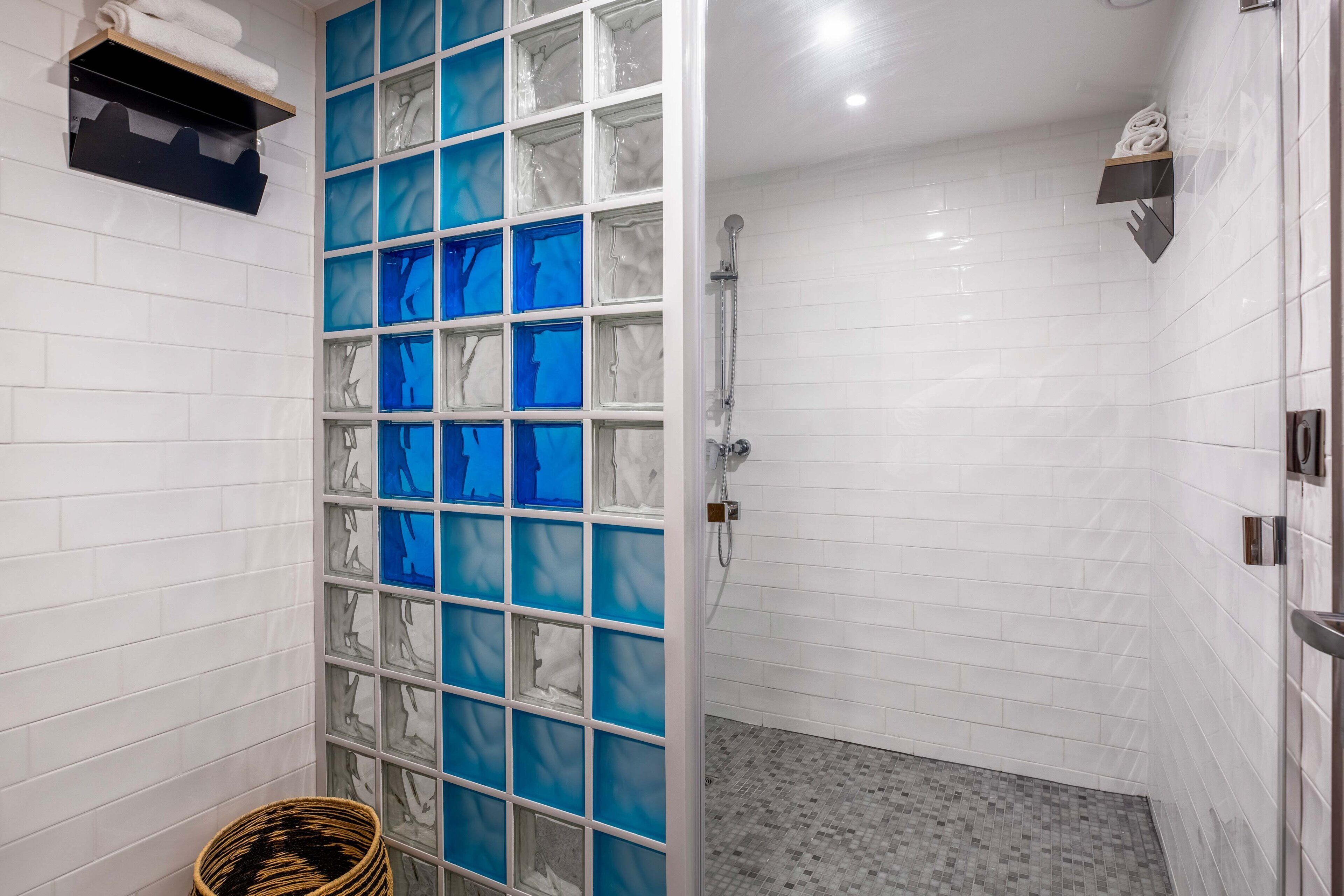 Une salle de bain avec des murs recouverts de carreaux blancs, un espace douche et une cloison en verre ornée de motifs bleus et blancs.