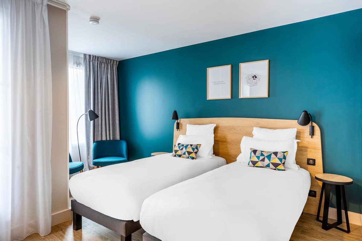 Ein Hotelzimmer mit zwei Betten, einem Schreibtisch, einem Stuhl und einem fenster mit Vorhängen.