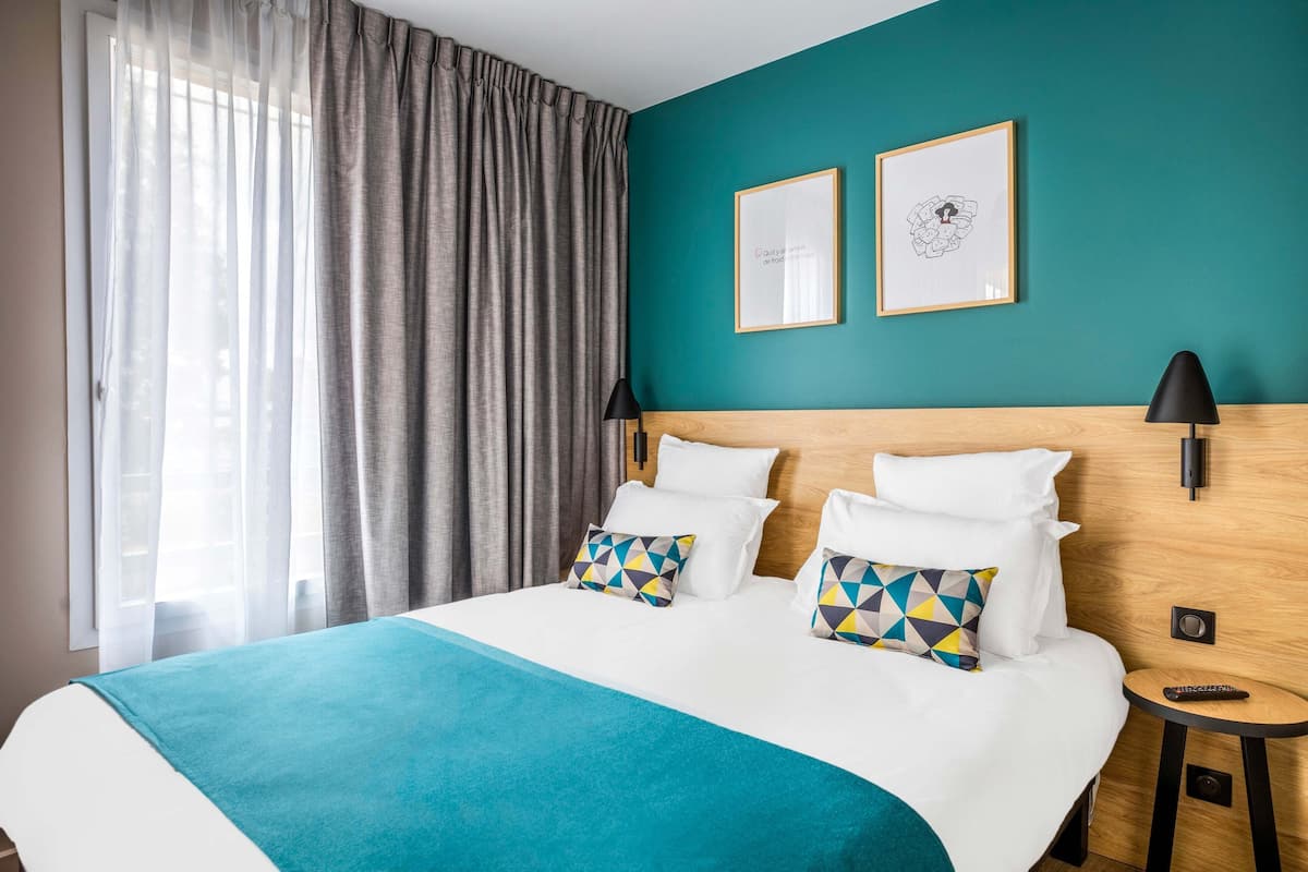 Ein Hotelzimmer mit einem großen Bett, zwei Kissen, einer türkisblauen Wand und einem gerahmten Bild.