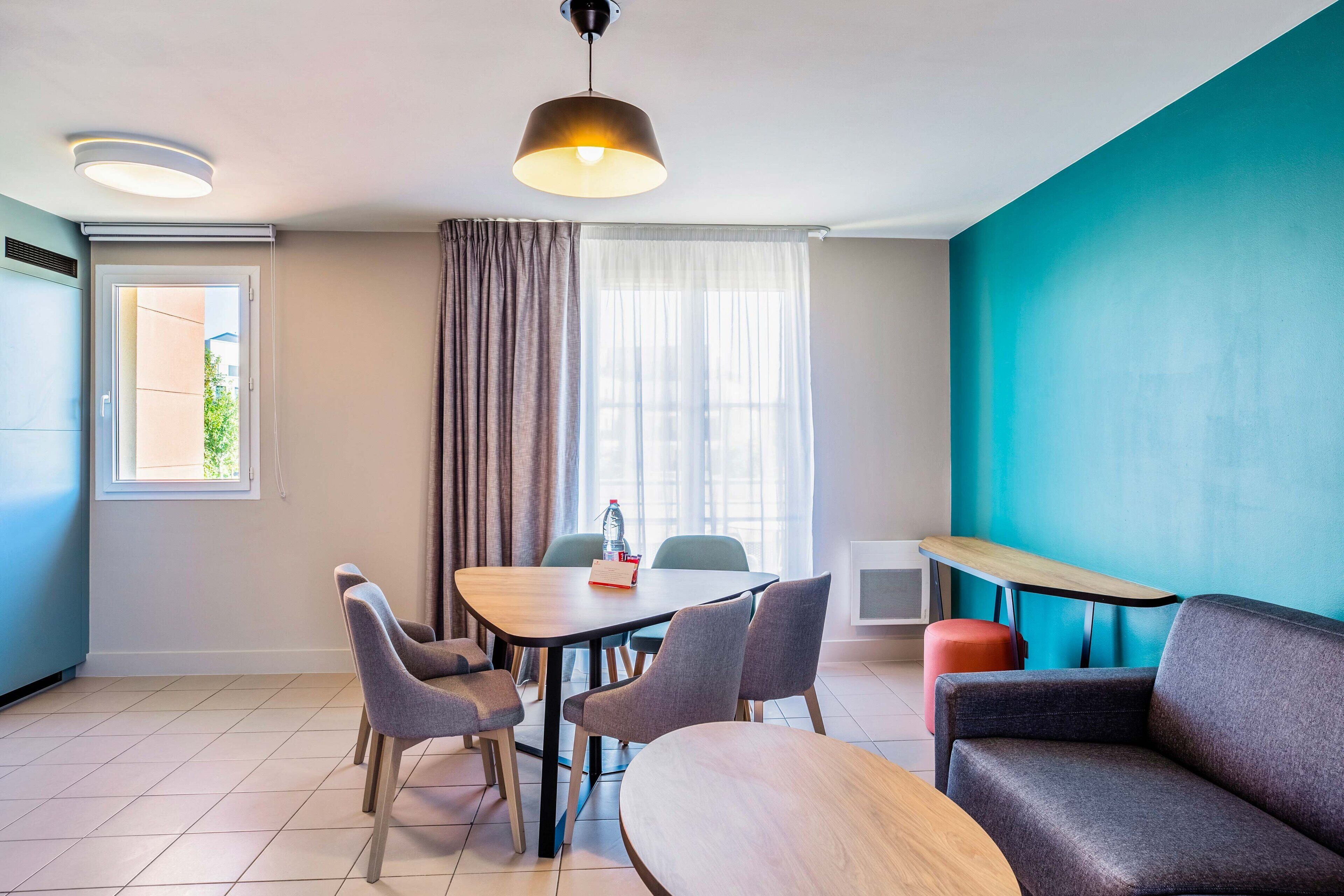 Una habitación moderna con una mesa de comedor, sillas, un sofá, una mesita auxiliar y una ventana con cortinas.