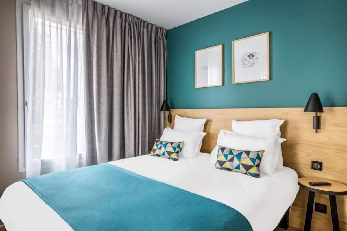 Ein Hotelzimmer mit einem Bett, zwei Wandlampen, einem Nachttisch und einem Fenster mit Vorhängen.