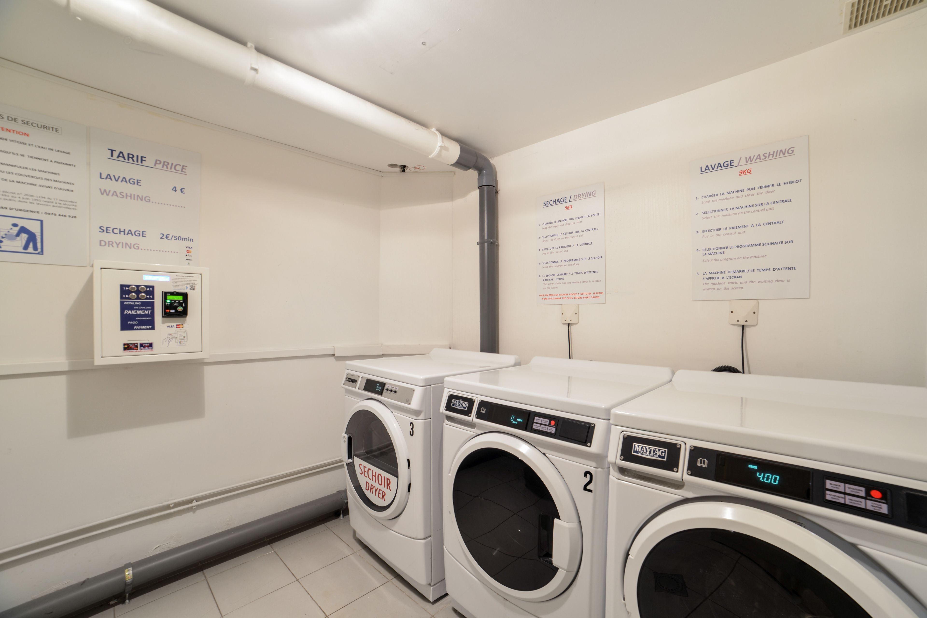 A laundry area with two washing machines, a payment terminal, and informational signs about tariffs and services.