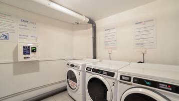 A laundry area with two washing machines, a payment terminal, and informational signs about tariffs and services.
