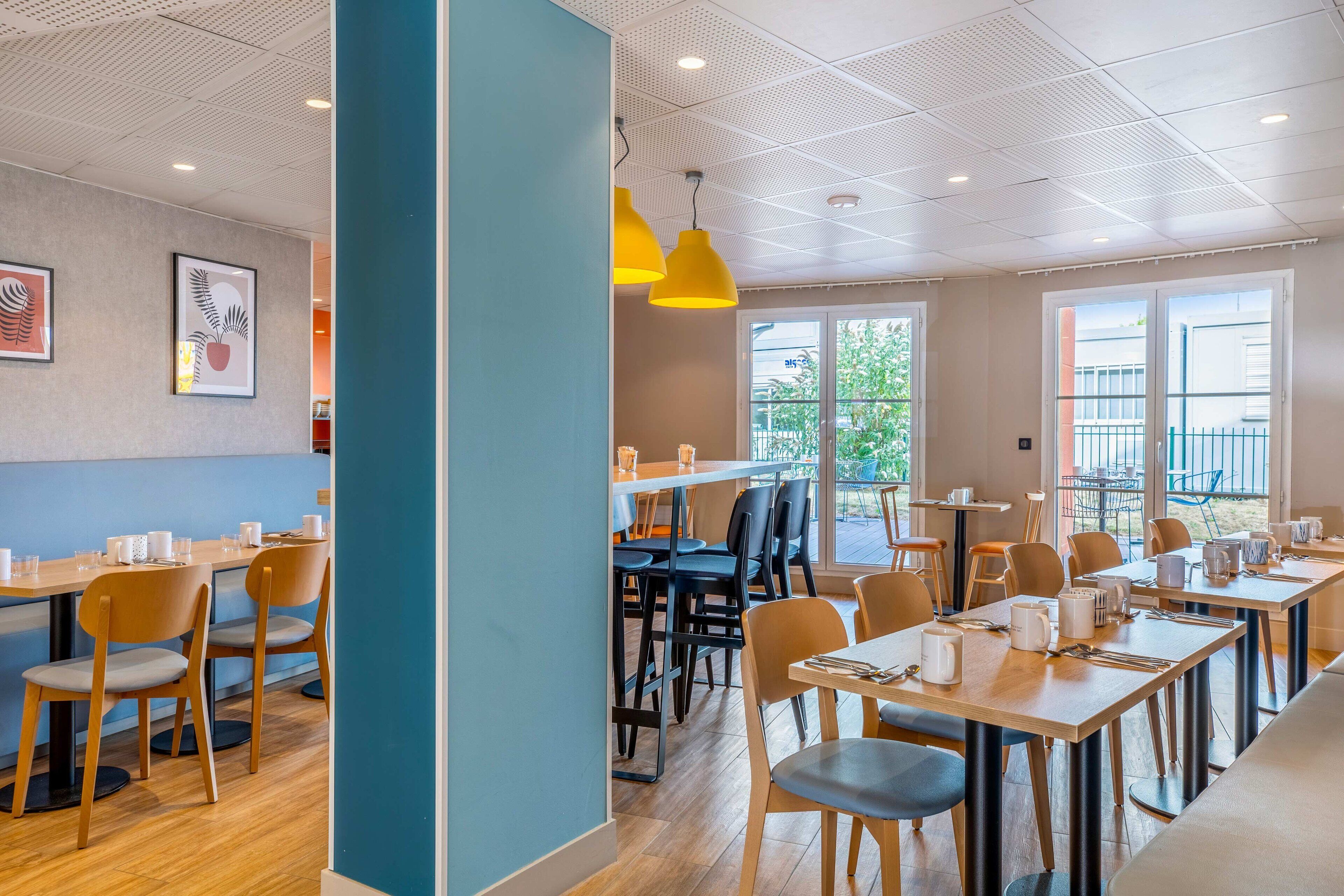 A modern dining area with wooden tables and chairs, yellow pendant lights, and framed artwork on the walls.