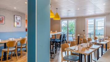 A modern dining area with wooden tables and chairs, yellow pendant lights, and framed artwork on the walls.