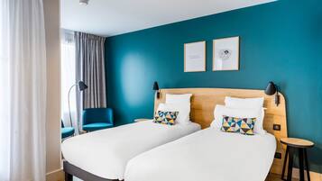 A hotel room with two beds, a blue accent wall, and a modern design.