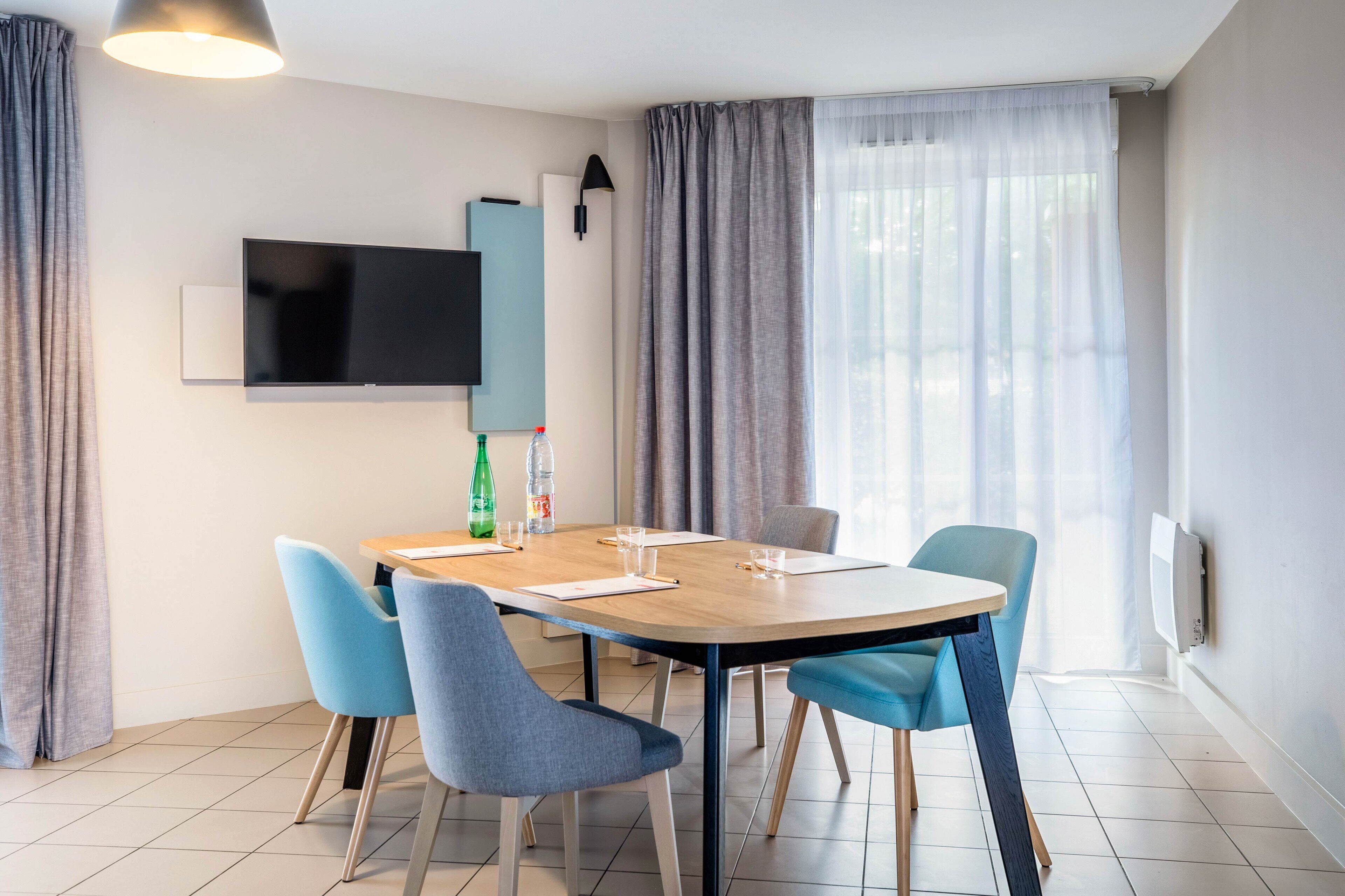 A modern dining area with a round table, four chairs, a flat-screen TV, and a bottle of water on the table.