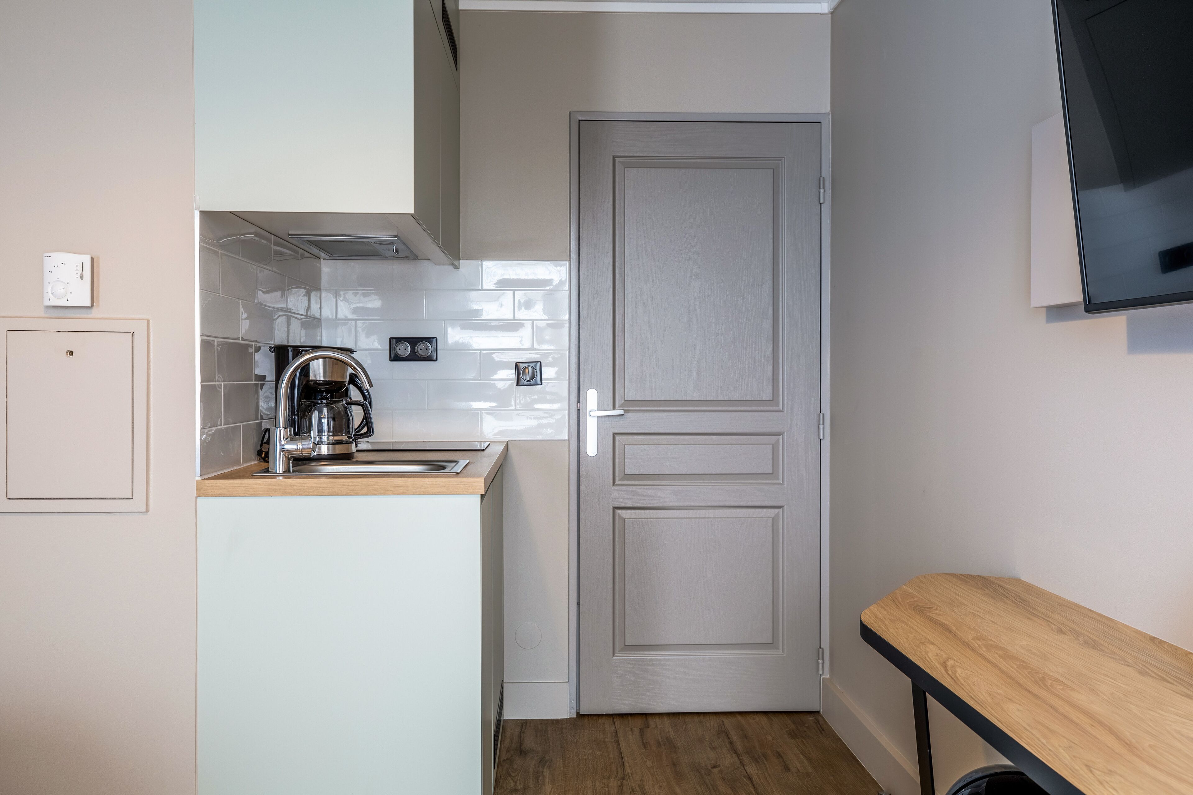 A compact kitchen with a coffee maker, a sink, and a door.