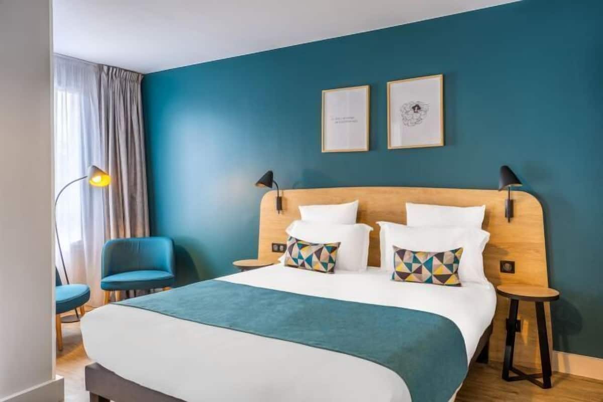 Ein Hotelzimmer mit einem Bett, zwei Stühlen, einem Schreibtisch und einer Lampe.