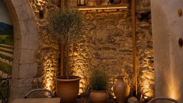 An outdoor patio with stone walls, wooden pergola, potted plants, and wicker furniture. - Hôtel du Midi (Visan)