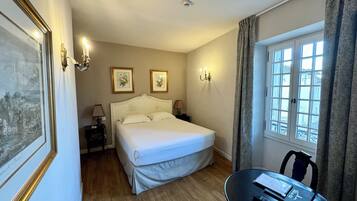A hotel room with a large bed, a small table with a remote control, and a window with curtains.
