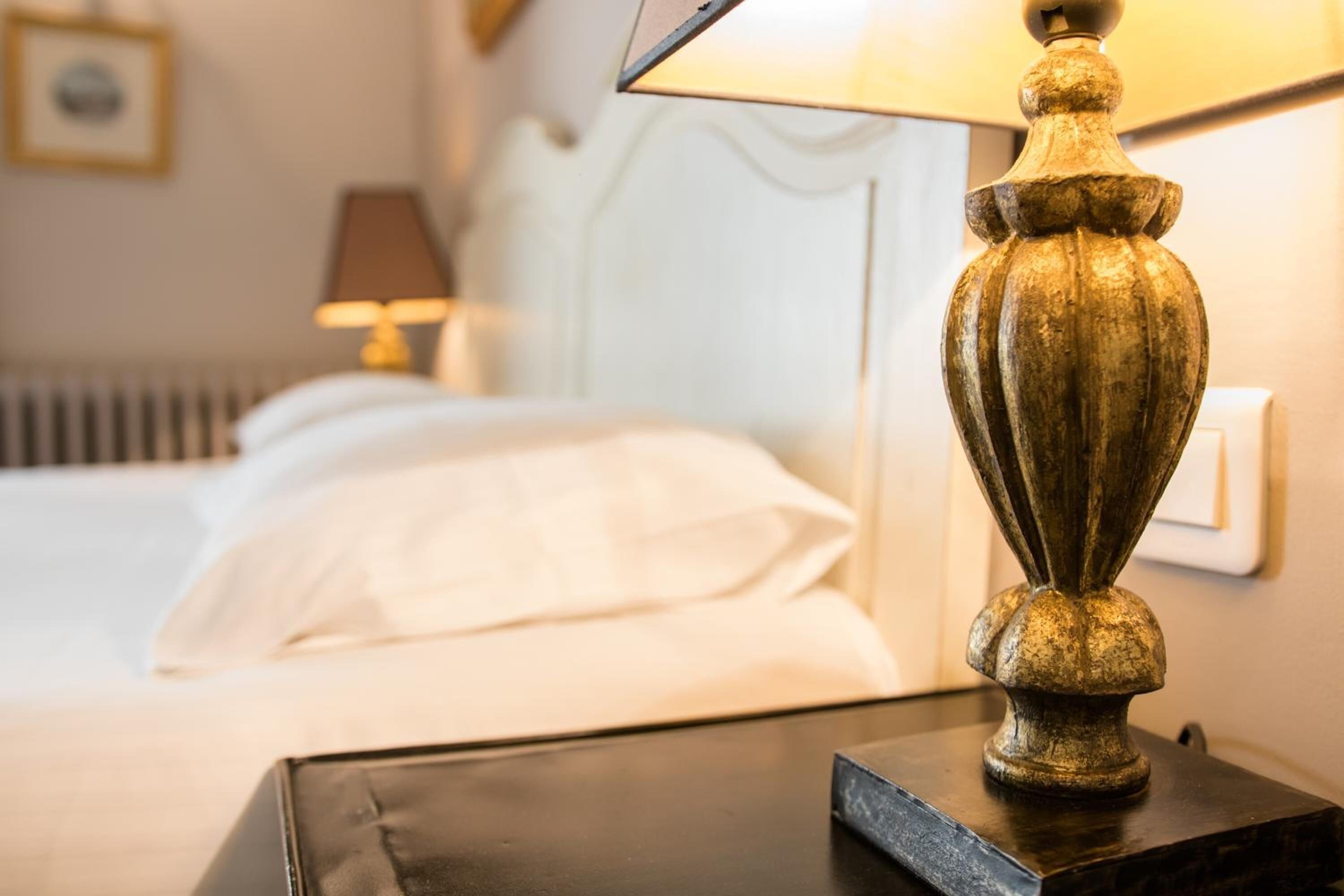 Een hotelkamer met een bed, een nachtkastje met een lamp en een lichtschakelaar op de muur.