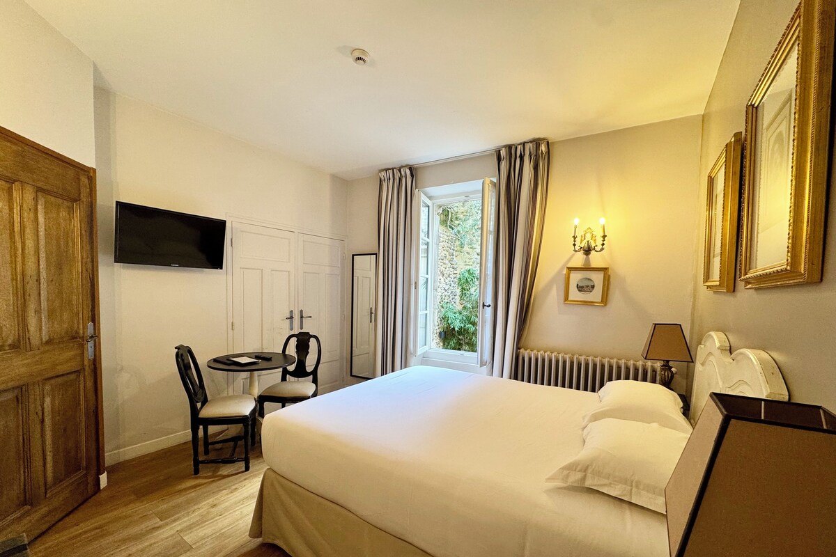 Habitación de hotel con una cama grande, un escritorio con silla, televisión, ventana con cortinas y un radiador.