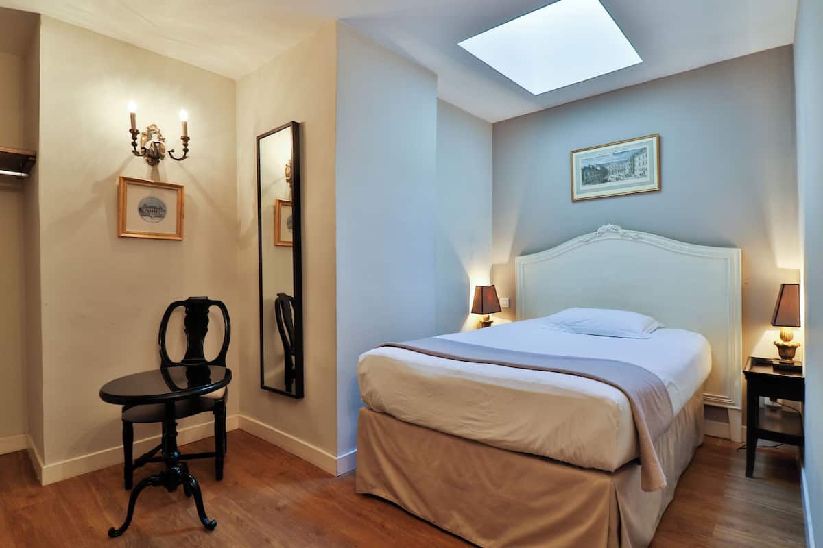A bedroom with a bed, bedside tables, a chair, a mirror, and a skylight.