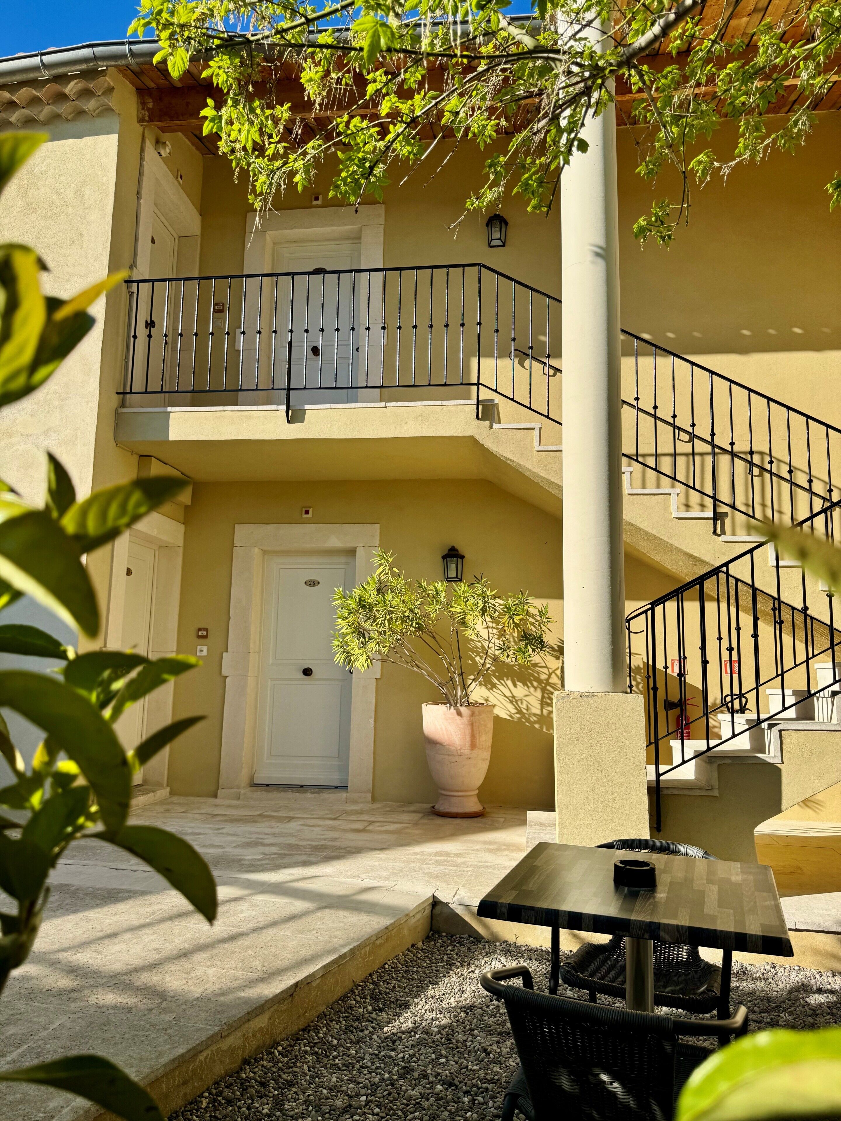 A building with a balcony, a staircase, a door, and a potted plant.