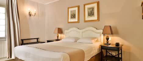 Una cama bien hecha con cabecera, dos mesitas de noche con lámparas y dos cuadros enmarcados en la pared.