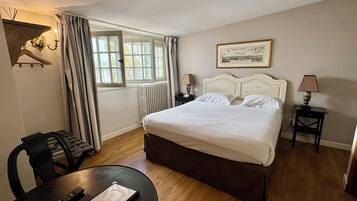 Une chambre d’hôtel avec un lit, une table avec une télécommande, une chaise, une lampe et une fenêtre avec des rideaux.