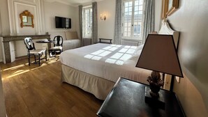 A hotel room with a large bed, a desk with a chair, a television, and a window with curtains. - Hôtel du Midi (Visan)