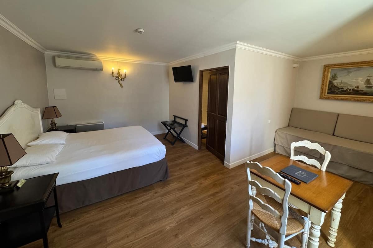 A hotel room with a large bed, a desk, a chair, a sofa, a television, and a painting on the wall.