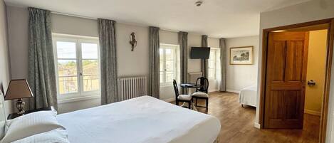 A hotel room with a large bed, a desk with a chair, a television, and a door leading to another room.
