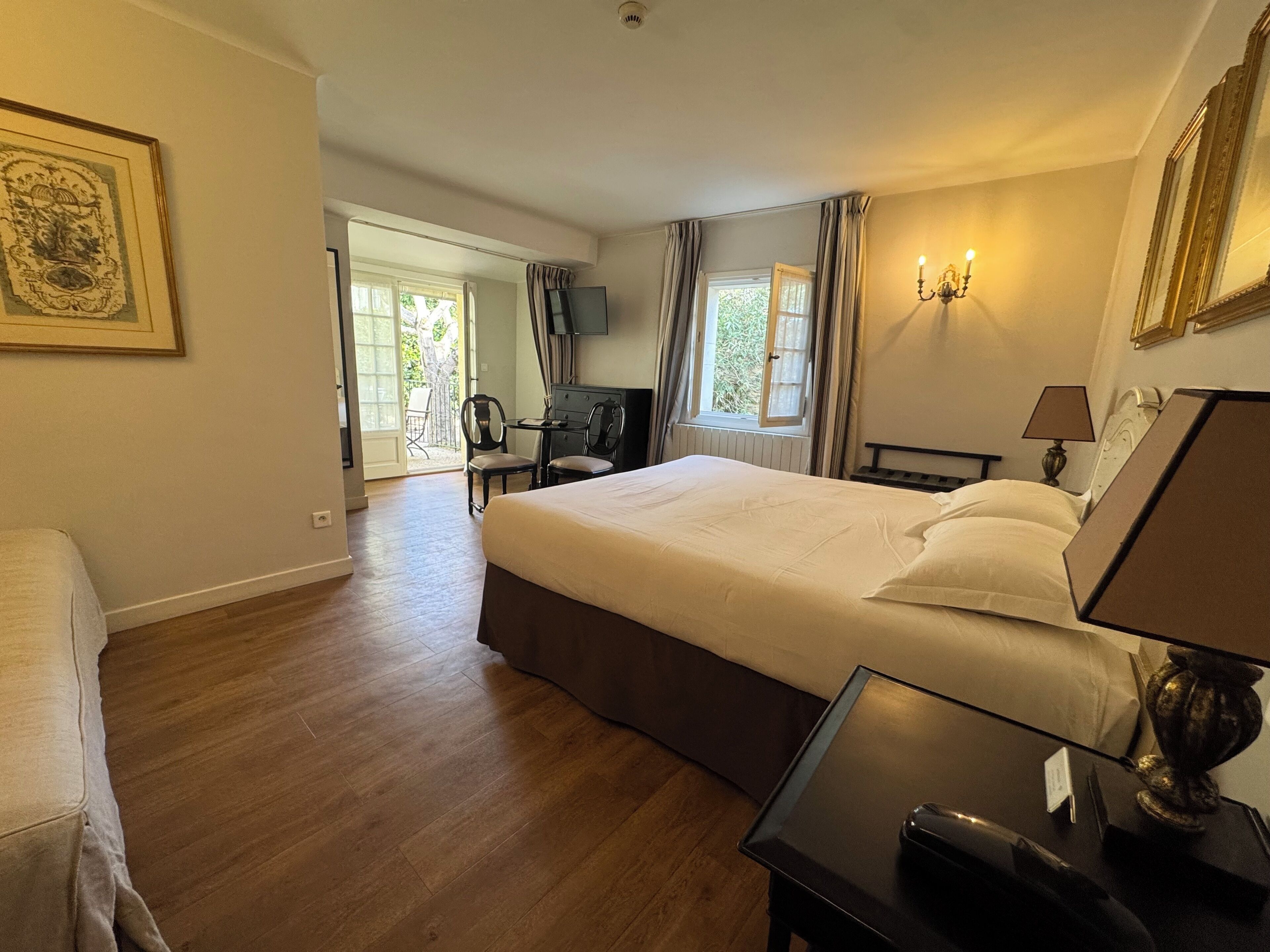 A hotel room with a large bed, a desk, a chair, a TV, and a window with curtains.