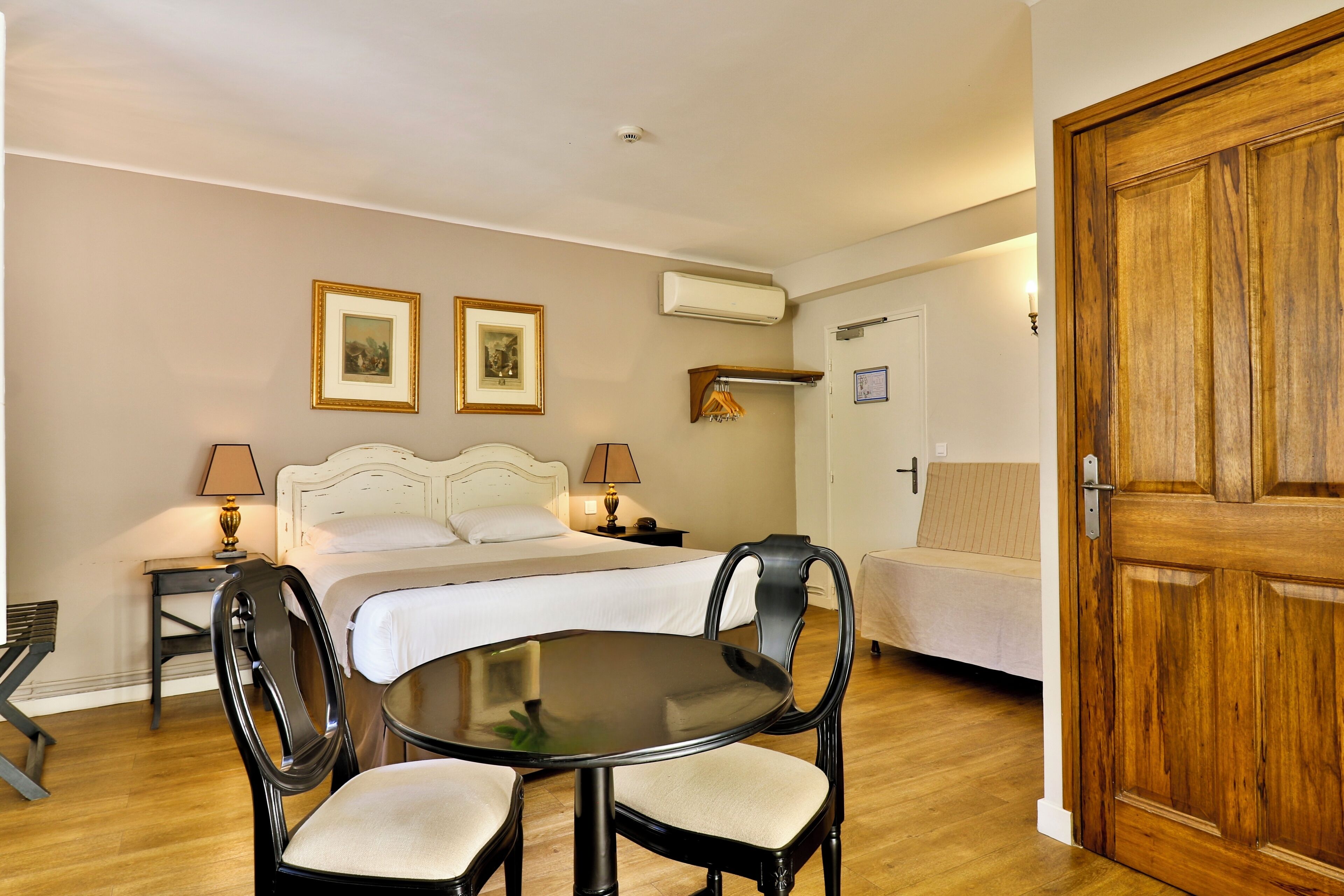 A hotel room with a bed, bedside tables, a round table with chairs, and a wooden door.